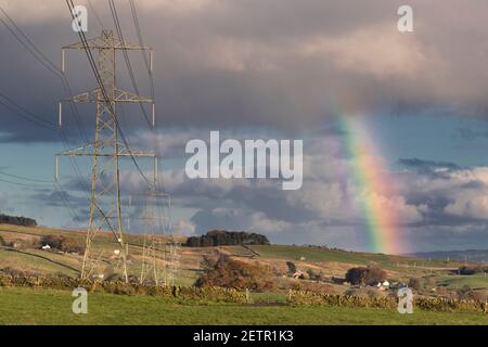 Eine Pylonlinie in der Nähe von Walltown Crags, Hadrian's Wall, wird von einem Regenbogen erhellt - Northumberland, Großbritannien Stockfoto