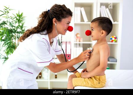 Doktor untersucht ihre Patientin mit Stethoskop, während sie beide eine Clownsnase tragen Stockfoto