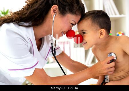 Doktor untersucht ihre Patientin mit Stethoskop, während sie beide eine Clownsnase tragen Stockfoto