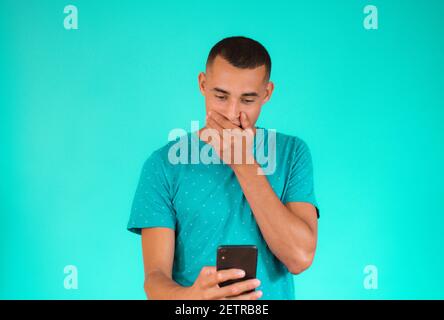 Überrascht junge lateinische Mann mit Handy über grünem Hintergrund. Stockfoto