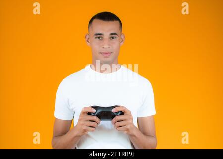 Fröhlicher junger Mann spielt die Konsole, Joystick über orangenen Hintergrund. Stockfoto