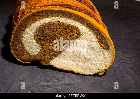 Ungewöhnlicher zweifarbiger frischer Laib Brot auf schwarzem Hintergrund, Foto in einer niedrigen Taste bei hartem Licht, Nahaufnahme Stockfoto