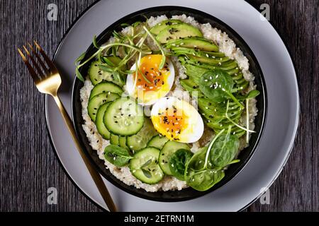 Quinoa Schüssel mit Ei, Sonnenblumen-Mikrogrün, Gurke, Avocado, Baby Spinat in einer schwarzen Schüssel auf einem dunklen Holztisch, flach liegend, Nahaufnahme, türkisch Stockfoto