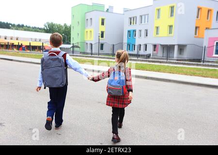 Kinder mit Aktentaschen über den Schultern auf dem Hintergrund der Schule. Stockfoto