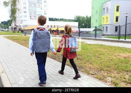 Kinder mit Aktentaschen über den Schultern auf dem Hintergrund der Schule. Stockfoto