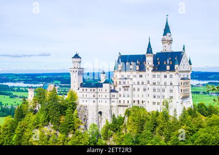 neuschwanstein, berühmtes Schloss der Märchen, Prinzessinnen und Liebenden, sticht vor dem blauen Himmel und den Wäldern vor der Kulisse der Seen hervor Stockfoto