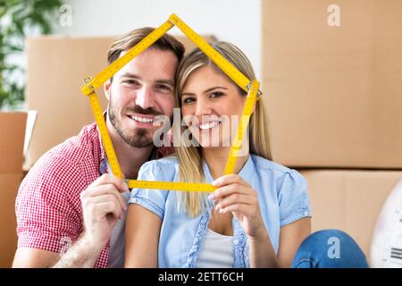Junges Paar zieht in ein neues Zuhause, hält Haus zusammen und lächelt zufrieden Stockfoto