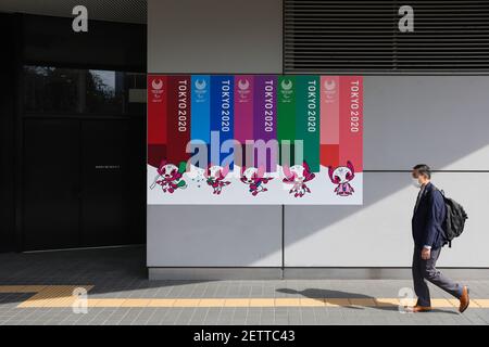 Tokio, Japan. März 2021, 01st. Ein Mann, der eine Maske trägt, als vorbeugende Maßnahme gegen die Verbreitung von covid-19, geht an einem Werbebanner der Olympischen Spiele 2020 in Tokio an einer Wand des Bunkyo Civic Center vorbei. Kredit: SOPA Images Limited/Alamy Live Nachrichten Stockfoto