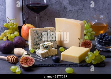 Blauer Käse und Parmesan auf einem schwarzen Brett, Obst, Wein und Honig. Nahaufnahme. Stockfoto