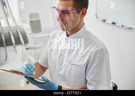 Arzt im Gesichtsschutz macht Notizen auf Papier Stockfoto