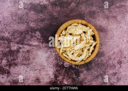 Ansicht von oben auf einer kastanienbraunen Tischplatte einer kleinen Holzschüssel, gefüllt mit panierten frittierten Zwiebeln. Stockfoto