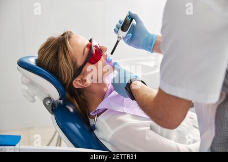 Qualifizierte Zahnarzt Behandlung weiblich in Sicherheitsbrille mit Photopolymer Lampe Stockfoto