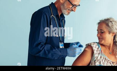 Arzt, der nach der Verabreichung eines Impfstoffs Pfandhilfe auf den Arm einer älteren Frau legt. Ältere Frau, die von einem Arzt geimpft wird. Stockfoto