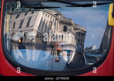 Wenige Tage bevor der Kanzler Rishi Sunak sein Budget liefert, spiegelt sich die verzerrte Architektur der Bank of England in der Windschutzscheibe eines Londoner Busses wider, der am 1st. März 2021 in London, England, durch die City of London, das Finanzviertel der Hauptstadt, fährt. Stockfoto