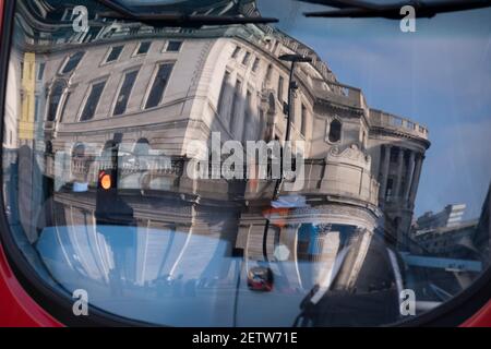 Wenige Tage bevor der Kanzler Rishi Sunak sein Budget liefert, spiegelt sich die verzerrte Architektur der Bank of England in der Windschutzscheibe eines Londoner Busses wider, der am 1st. März 2021 in London, England, durch die City of London, das Finanzviertel der Hauptstadt, fährt. Stockfoto