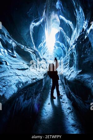 Silhouette des Fotografen mit Kamera und Rucksack macht Bilder Von erstaunlichen Gletschereishöhle in den Bergen von Kasachstan Stockfoto