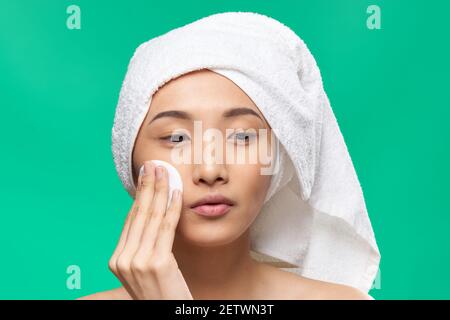Frau mit einem Handtuch auf dem Kopf wischt ihr Gesicht Mit einem Wattepad Grün Hintergrund Stockfoto