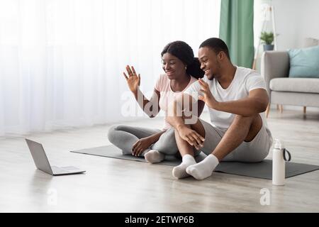 Fröhliche afroamerikanische Paar mit Online-Yoga-Klasse, Gruß Trainer Stockfoto