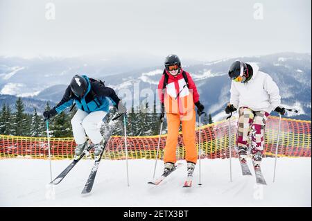 Die ganze Länge der Skifahrer Team in Skijacken und Helme Skifahren in Winter verschneiten Bergen, machen Sprung, während gleiten schneebedeckten Piste auf Skiern. Konzept der Wintersport-Aktivitäten und Freundschaft. Stockfoto