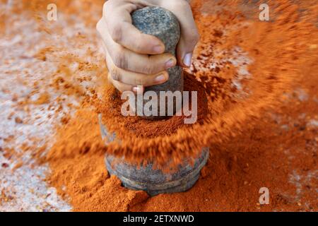 Indische Frau Handpudering indische Gewürze Red Chilly, Chili Paprika Pulver Spritz Explosion mit Steinmörtel indische Küche Kerala Indien Sri Lanka Stockfoto