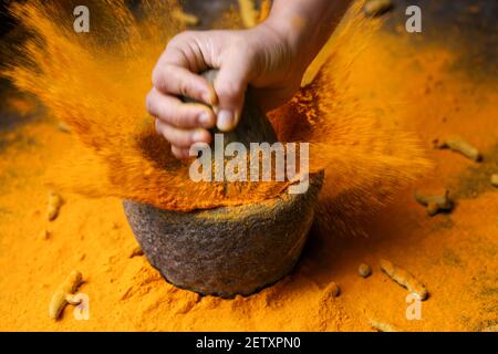 Frau Handpudering indischen Gewürzen Kurkuma Pulver Spritzer Explosion Stein Mörser Kerala Indien Sri Lanka traditionelle indische Küche Masala für Curry Stockfoto