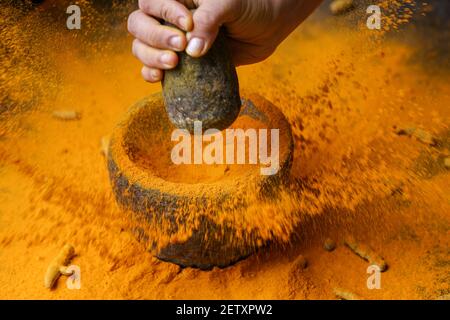 Frau Handpudering indischen Gewürzen Kurkuma Pulver Spritzer Explosion Stein Mörser Kerala Indien Sri Lanka traditionelle indische Küche Masala für Curry Stockfoto