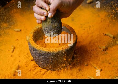 Frau Handpudering indischen Gewürzen Kurkuma Pulver Spritzer Explosion Stein Mörser Kerala Indien Sri Lanka traditionelle indische Küche Masala für Curry Stockfoto