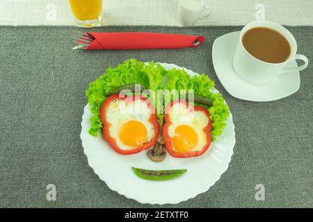 Rührei, Spiegeleier, mit Gemüse in Form eines fröhlichen Gesichts. Zwei Spiegeleier mit Paprika und grünen Erbsen in Form eines Smiley Stockfoto
