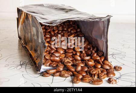 Kaffeebohnen werden aus einer offenen Packung auf dem Tisch verschüttet. Nahaufnahme Stockfoto