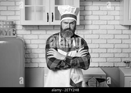 Schöner bärtiger Koch in weißer Uniform und Hut mit langem, üppigen Schnurrbart auf ernsthaftem Gesicht stehend und Händen zusammengeschraubt. Stockfoto