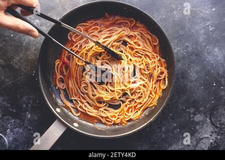 Tomatenpasta wird in einer Pfanne auf dem Hintergrund der Küche gekocht. Italienische Pasta Hintergrund. Italienisches Essen und Küche Konzept. Hochwertige Fotos Stockfoto