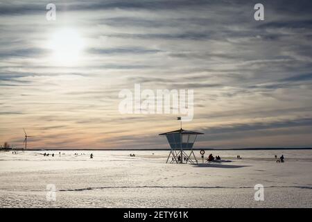 Die Hütte des Rettungsschwimmer steht in Wache, während die Menschen einen schönen Wintertag am Meer genießen. Das Meer ist gefroren und der Strand ist Bucht Stockfoto