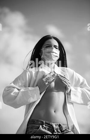 Junge Frau, die sich vor dem Corona Virus schützt, covid 19 mit einer Maske auf blauem Himmel Hintergrund. Stockfoto