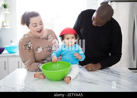 Ein glückliches interrassisches Paar in einer modernen Küche mit ihrem kleinen Mädchen. Stockfoto