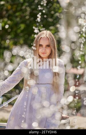 Hübsche blonde Frau in weißem Kleid mit Fahrrad in der Nähe Brunnen Bei sonnigem Licht Stockfoto