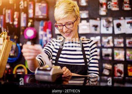 Schöne fröhliche Frau, während sie einen Scheck an der Kasse auszog. Stockfoto