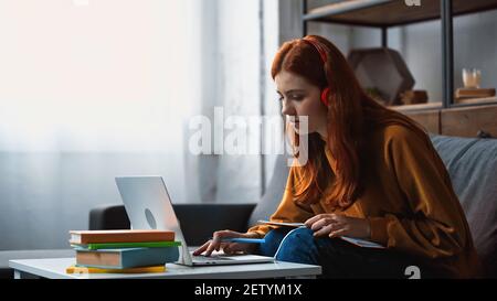 Schüler in Kopfhörer mit Laptop in der Nähe von Büchern auf verschwommenem Vordergrund Stockfoto