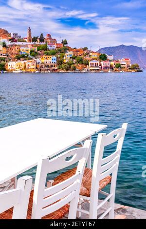 Symi, Griechenland. Typisch griechische Taverne weiße Stühle mit Tischen, Meer auf Rhodos. Stockfoto