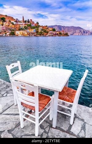 Symi, dodekanesische Inseln in Griechenland. Weiße Stühle mit Tischen in typisch griechischer Taverne am Meer auf Rhodos. Stockfoto