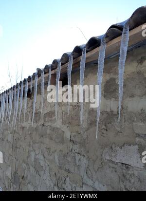 Eiszapfen in einer Reihe hängen vom Dach eines Ziegelhauses. Stockfoto