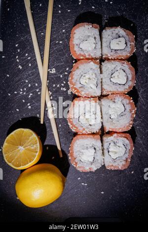 Sushi-Brötchen mit Zitrone und Souce auf schwarzem Brett auf dunklem Hintergrund. Flache Anordnung auf schwarz, Draufsicht Stockfoto