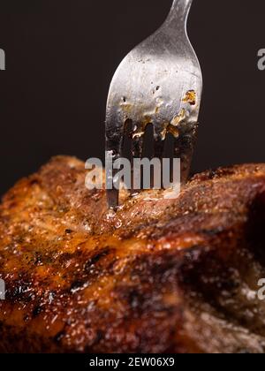 Gabel in einem gebratenen Stück Fleisch, saftiges Schweinefleisch Nahaufnahme Stockfoto