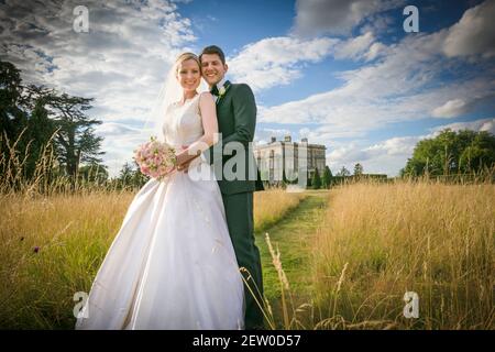 Braut und Bräutigam glücklich zusammen im langen Grasfeld eines großen Anwesens. Stockfoto