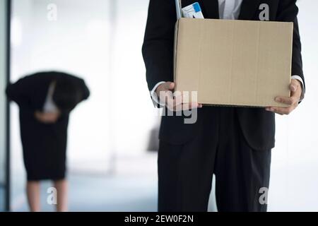 Gefeuert Geschäftsmann mit Box von Habseligkeiten, Kollege im Hintergrund Stockfoto