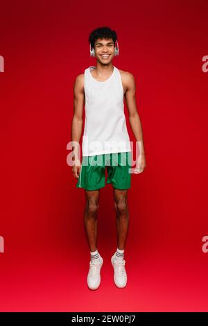 In voller Länge glücklicher afroamerikanischer Mann in kabellosen Kopfhörern Springt auf Rot Stockfoto