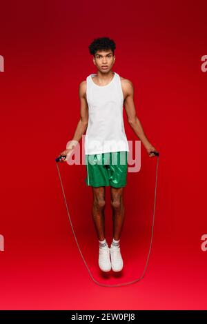 Volle Länge des sportlichen afroamerikanischen Mannes in grünen Shorts Arbeiten mit Springseil auf rot Stockfoto