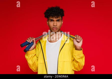 Durchbohrter afroamerikanischer Mann in gelber Jacke mit Springseil Auf rot Stockfoto