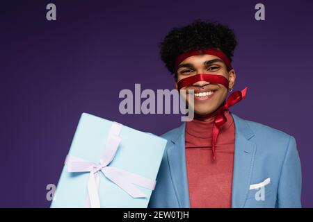 Fröhlicher afroamerikanischer Mann mit Band nahe Gegenwart auf gebunden Violett Stockfoto