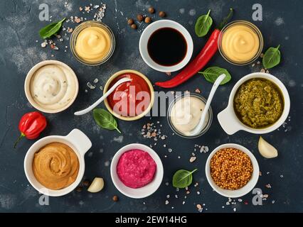 Set von Saucen in Schüsseln - Ketchup, Mayonnaise, Senf, Sojasauce, bbq-Sauce, Pesto, Chimichurri, Senfkörner auf dunklem Steingrund. Obersicht Cop Stockfoto