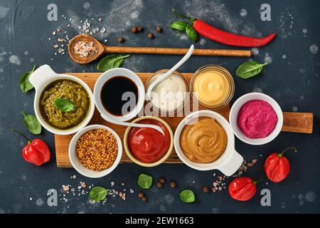 Set von Saucen in Schüsseln - Ketchup, Mayonnaise, Senf, Sojasauce, bbq-Sauce, Pesto, Chimichurri, Senfkörner auf dunklem Steingrund. Obersicht Cop Stockfoto